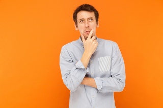 Hmm, i'm need thinking. Young adult man looking up, holding chin and musing. Indoor shot. Isolated on orange background