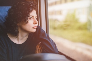 Sad young woman is traveling economy class on a train sitting and contemplating and looking out through the window