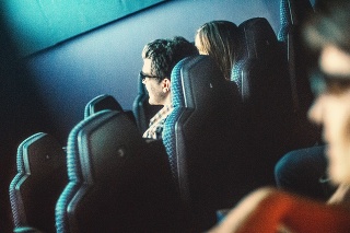 Rear view of people enjoying a 3-d movie at movie theater. Some seats are empty. One couple is in sharp focus.