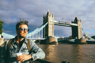 Young man walking on the streets of London, enjoying the view by the river Thames, wearing a denim jacket and a backpack.