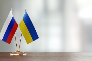 Russian and Ukrainian flag pair on desk over defocused background. Horizontal composition with copy space and selective focus.