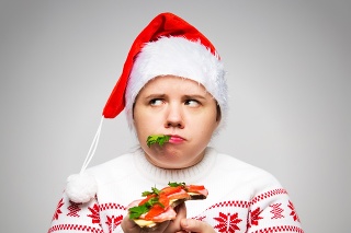 Portrait of a fat woman with a large sandwich in her hands. She is wearing a festive Christmas sweater and Santa hat. Overeating on holidaysPortrait of a fat woman with a large sandwich in her hands. She is wearing a festive Christmas sweater and Santa hat. Overeating on holidays