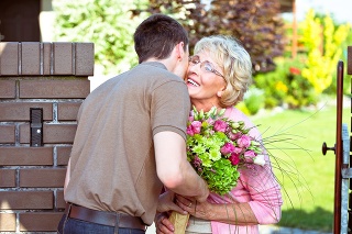 Outdoor picture of grandson giving flowers to his happy grandmother.