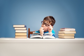 seven years old child reading a book at home. Boy studing at table on blue background
