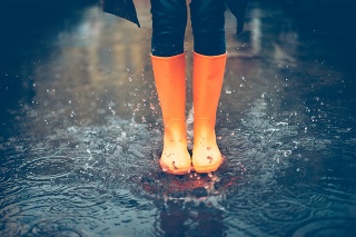 Close-up of woman in orange rubber boots jumping on the puddle
