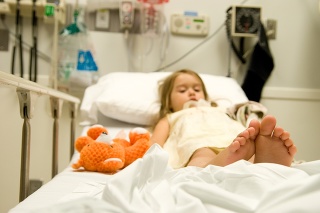 This little girl just got 6 stitches in the chin. Her feet are in focus on top of the hospital bed.