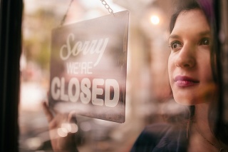 A thoughtful woman looking out window, turns closed sign on glass front door of coffee shop with reflection of street in glass