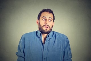 Closeup portrait young handsome man shrugging shoulders who cares so what I don't know gesture isolated on grey wall background. Body language expression. Man showing ignorance