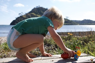 A Toddler plays with his toy by the Beach in summer. Taken in a small beach Bach town in New Zealand's North Island.