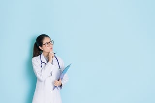 successful pretty woman clinic doctor holding pen and patient medical records looking at empty area thinking illness solution standing in blue wall background.