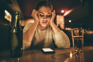 Depressed woman sitting in a bar and looking at her cell phone while waiting for a call from her boyfriend.