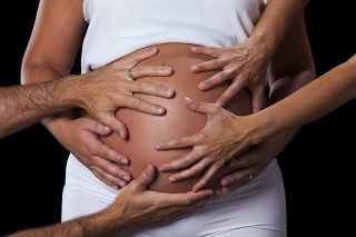 Many hands caressing a pregnant belly isolated on black
