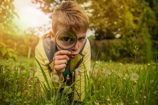 Little boy outdoors exploring with a magnifying glass