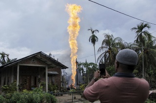 Muž si fotí mobilným telefónom požiar na ropnom vrte v dedine Pasir Putih v indonézskej provincii Aceh.