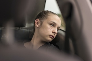 Emotional portrait of a teenage girl looking troubled, worried inside a car looking through the window on a rainy day, appearing to be lost in a daydream.