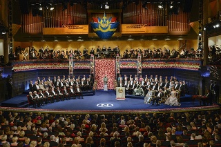 Na scéne vľavo sedí desať laureátov Nobelovej ceny a vpravo švédska kráľovská rodina na čele s kráľom Karlom XVI. Gustávom.
