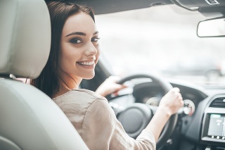 Rear view of attractive young woman in casual wear looking over her shoulder while driving a car