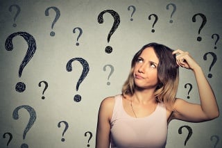 Thinking young woman looking up at many question marks isolated on gray wall background