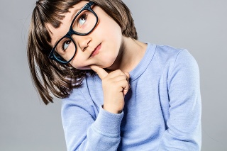 thoughtful beautiful little girl with serious eyeglasses holding her head to imagine, think, hesitate or have an intelligent idea or solution, grey background studio