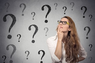 Thinking business woman with glasses looking up at many question marks isolated on gray wall background