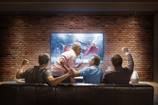 :biggrin:A group of adult male friends are cheering while watching Ice Hockey game at home. They are sitting on a sofa in the modern living room faced to a big TV set on the front wall.