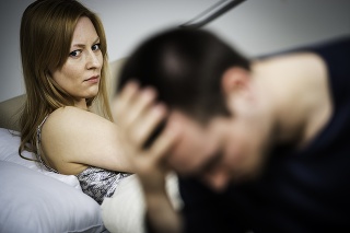 Depressed mature man holding hand on head while sad woman sitting in background, focus on woman.