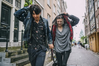 Couple holding hands making a dash for cover as it is raining. Laughing they hold their jackets over their heads.