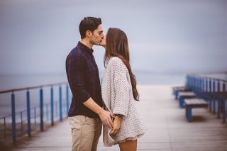Romantic boyfriend and girlfriend tenderly giving a kiss on a pier next to the sea.