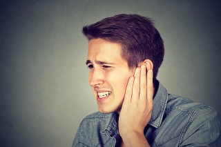 Tinnitus. Closeup up side profile sick male having ear pain touching his painful head isolated on gray background