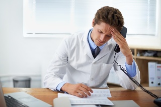 Shot of a concerned doctor sitting in his office and talking on the phone while looking over paperwork