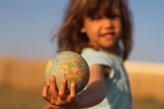 Front view of a child hand holding a damaged toy globe, shallow depth of field
