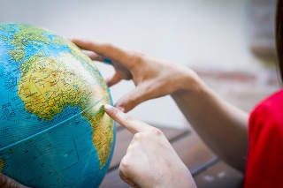 A young person (not recognizable) points the finger on Africa while another person (not recognizable) holding the earth globe. They are choosing a place to vacation or they are young students who are studying geography.