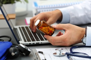 Male medicine doctor hands hold jar of pills and type something on laptop computer keyboard. Panacea and life save, prescribing treatment, legal drug store, take stock, consumption statistics concept