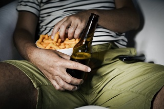 closeup of a young caucasian man drinking beer and eating cheese puffs while is watching the television