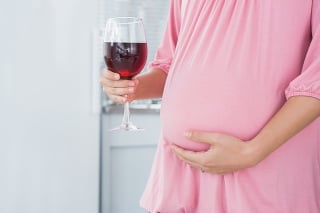 Expecting woman in her kitchen with red wine in right hand