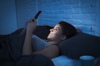 young beautiful womanl in bed using mobile phone late at night at dark bedroom lying happy and relaxed enjoying social media network at her phone in communication internet addiction concept