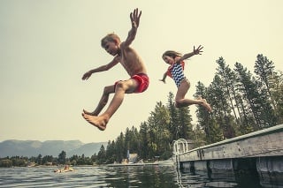A little boy and little girl jumping off the dock into a beautiful mountain lake. Having fun on a summer vacation