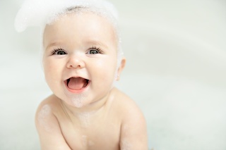 Baby girl bathes in a bath with foam and soap bubbles
