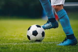 Close up of legs and feet of football player in blue socks and shoes running and dribbling with the ball. Soccer player running after the ball. Sports venue in the background
