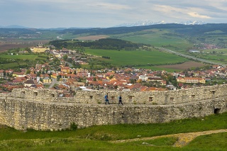 Turisti na hradbách spodného nádvoria Spišského hradu, dole Spišské Podhradie, vľavo hore Spišská Kapitula a na horizonte sa vypínajú štíty Vysokých Tatier.