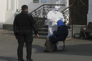 Policajt dohliadajúci na testovanie staršej žobráčky na ochorenie COVID-19 v Kyjeve.