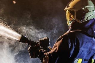 Side view of a firefighter in full gear operating a fire hose in a smokey area.