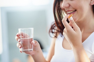 Shot of a young woman taking a pill with a glass of water during her morning routine at home