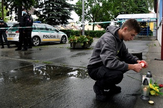 Chlapec s policajtmi za chrbtom zapaľuje sviečku.