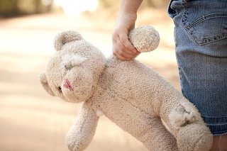 Color stock photo of a little runaway girl holding an old teddy bear at the side of a dirt road in the rural country.
