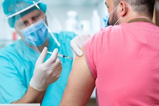 Doctor wearing protective visor and surgical gloves injecting COVID-19 vaccine into patient's arm