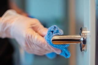 Closeup of the hands of a person disinfecting a door knob.
