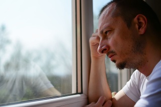 Indoor close-up image of disturbed, sad, Caucasian, mid adult man. Sad young man looking through the window. Feeling hopeless.