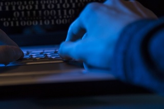 Unrecognizable computer hacker commits a cyber attack using his laptop computer in home office or business office.   Or computer programmer at work.  Computer coding on screen.
