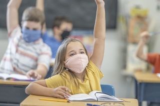 Group of students wearing protective face masks while raising their hands in class.